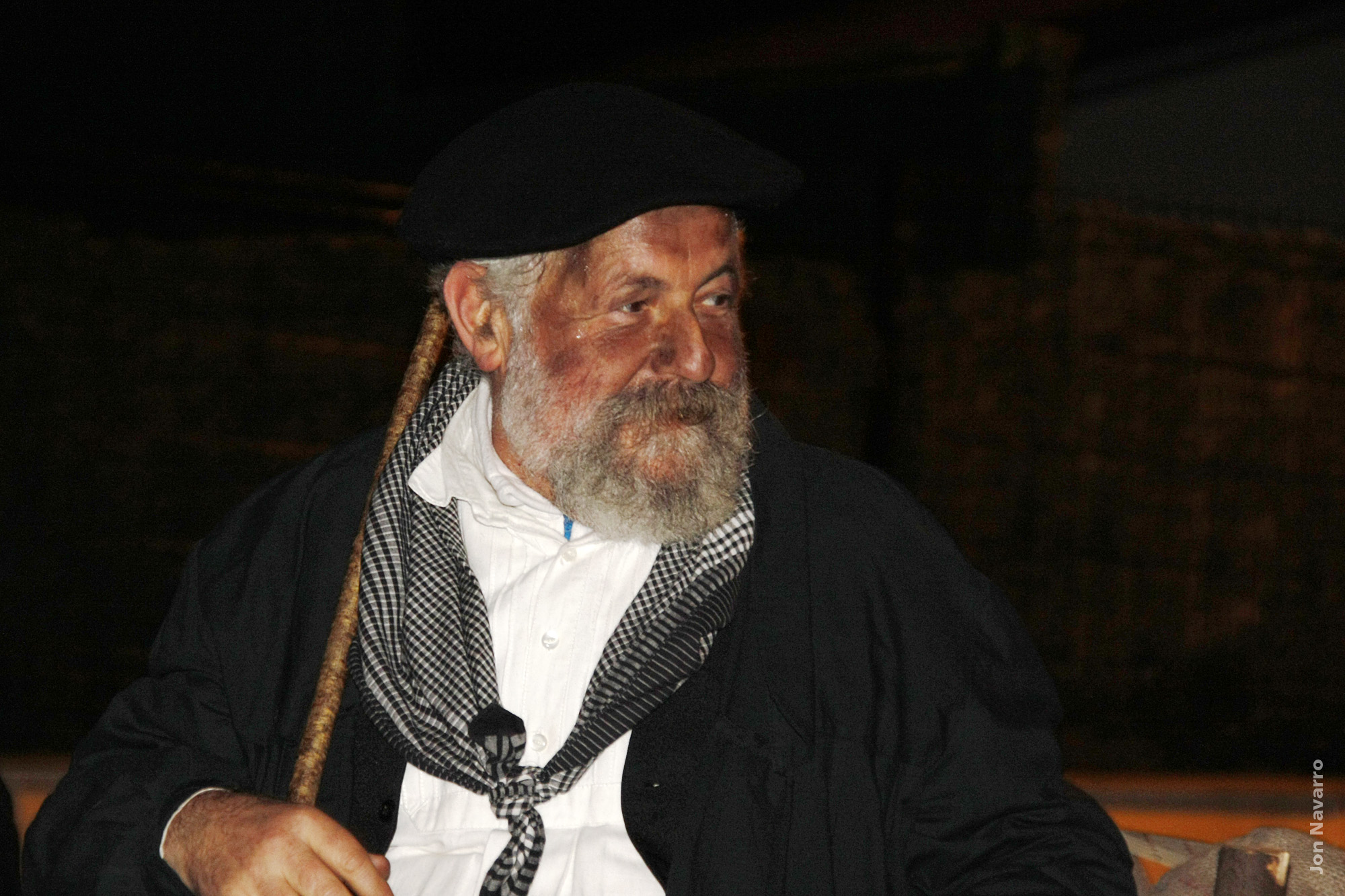 Olentzero sentado de noche, con boina, pañuelo de cuadros y bastón, en el desfile de Arakaldo